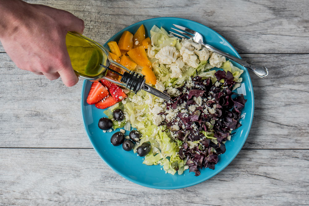 plate with vegetable mix and person's hand adding olive oil, top view